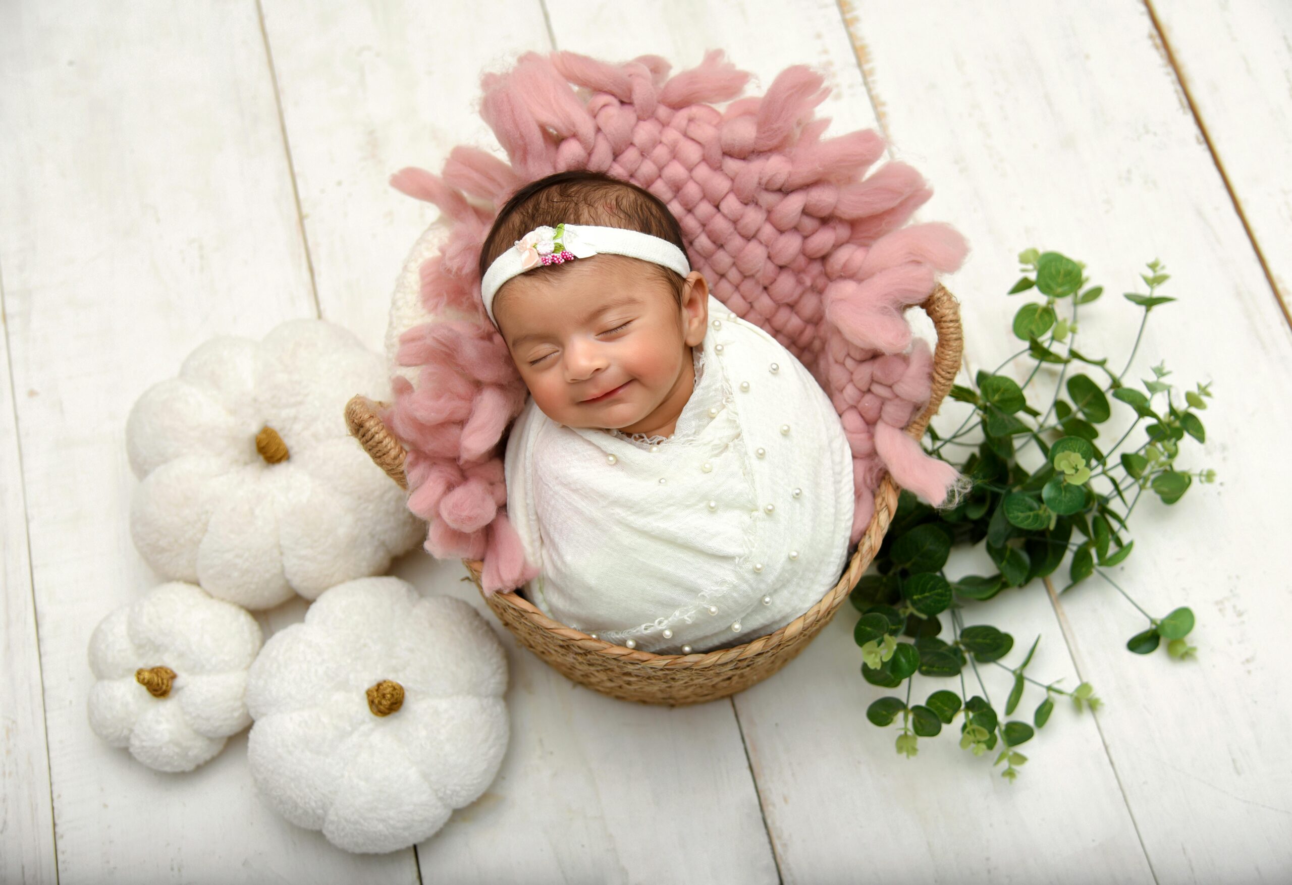 Charming newborn sleeping in a basket with cozy textures and natural elements around.