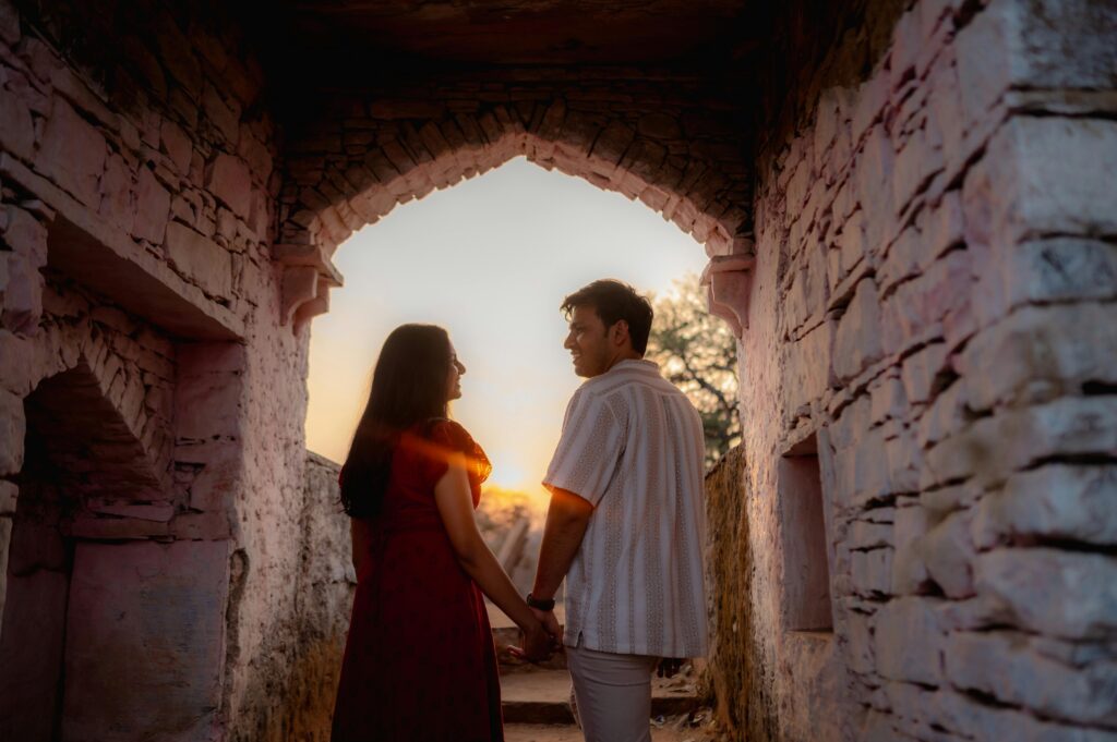 A romantic couple holds hands under an ancient archway at sunset, exuding peaceful love and connection.