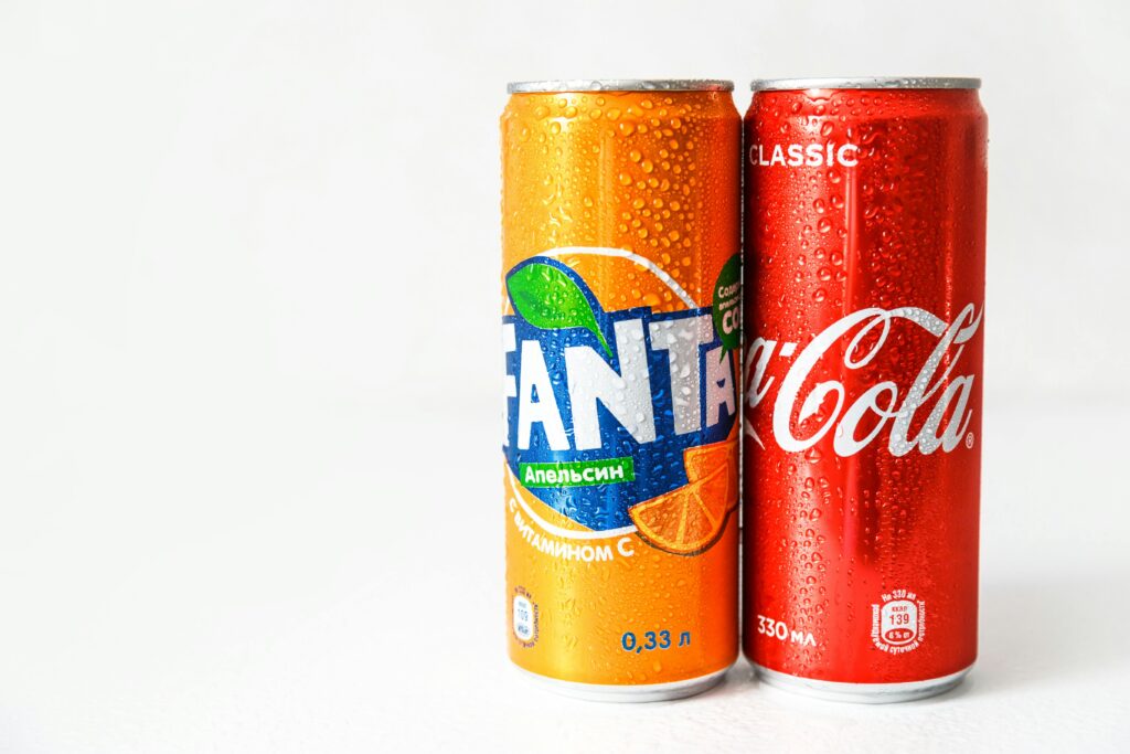 Close-up image of refreshing Coca-Cola and Fanta cans with water droplets.